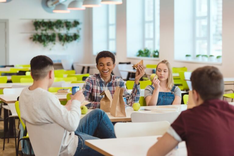 kids in a cafeteria smiling with packed lunches on the table