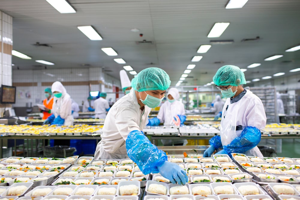 two people wearing protective gear while packing food in a facility
